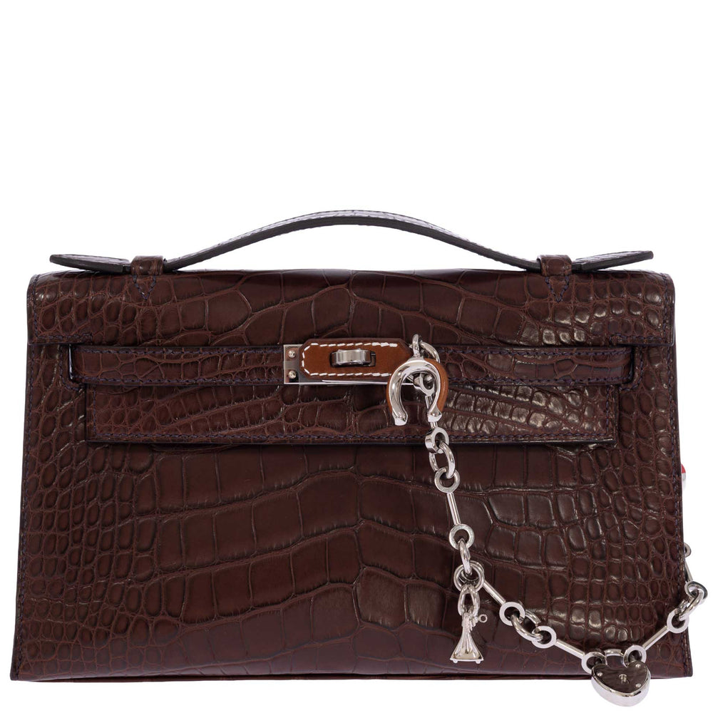 Hermès Kelly Pochette in Havane matte alligator, front view styled with a silver charm chain sold separately.