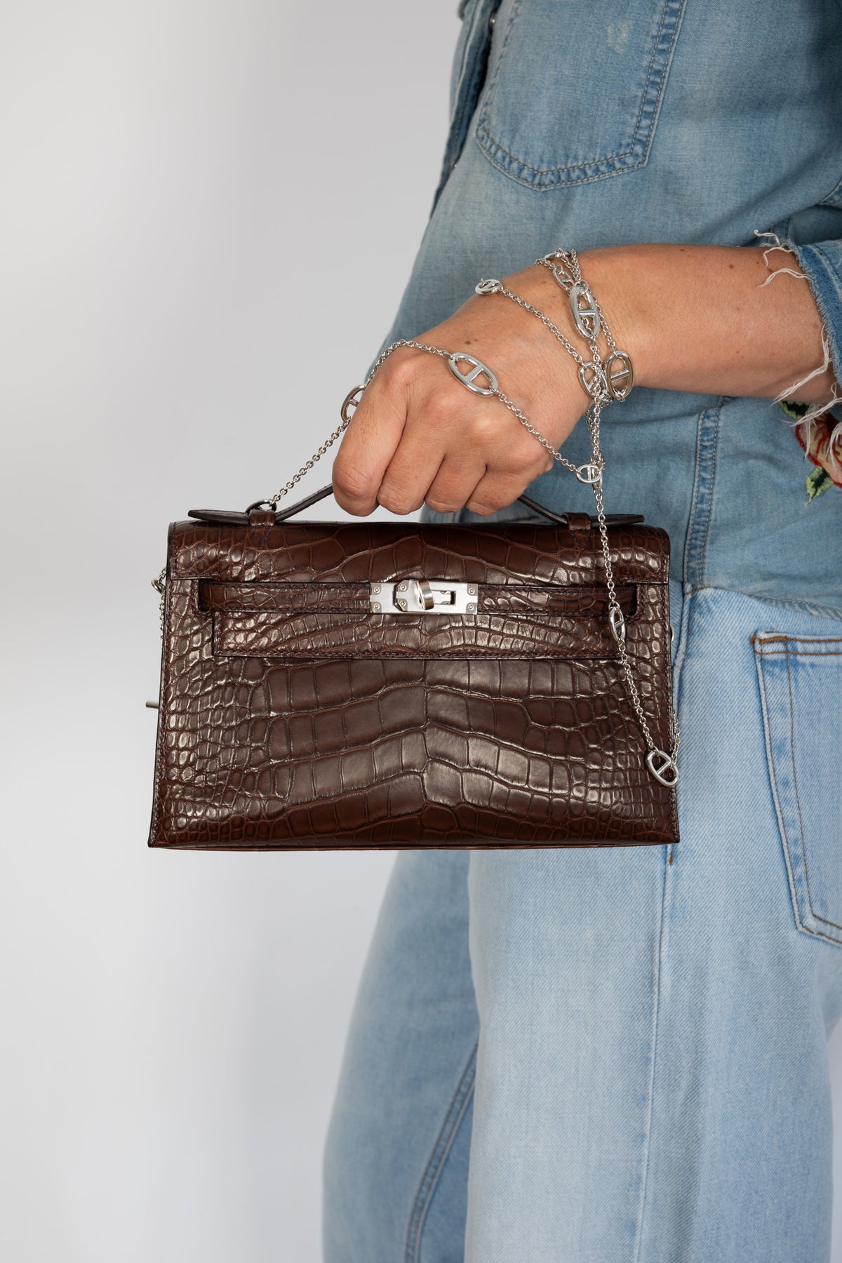 Hermès Kelly Pochette in Havane matte alligator, carried by the top handle, close view.