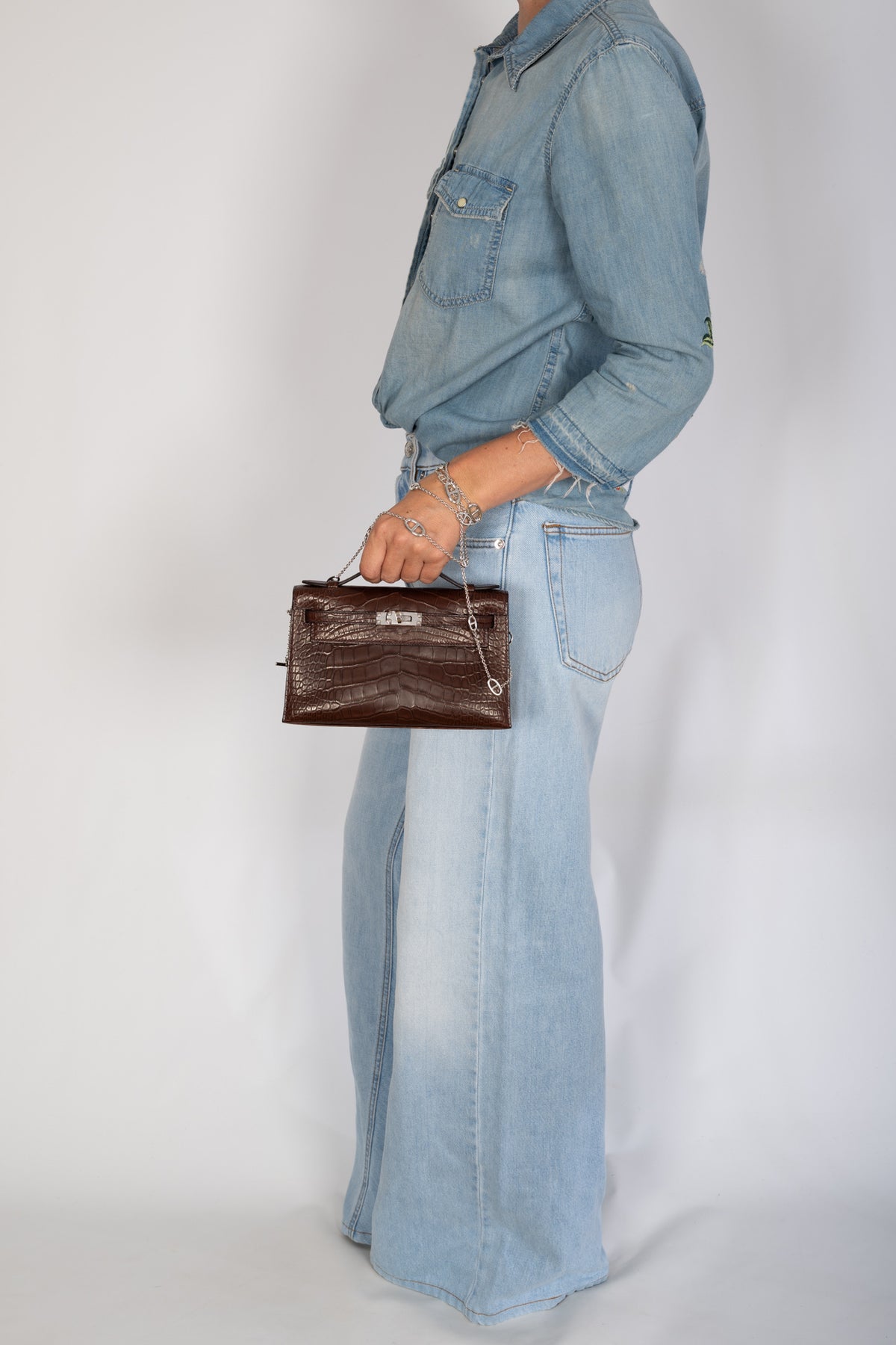 Hermès Kelly Pochette in Havane matte alligator, carried by the top handle with denim.