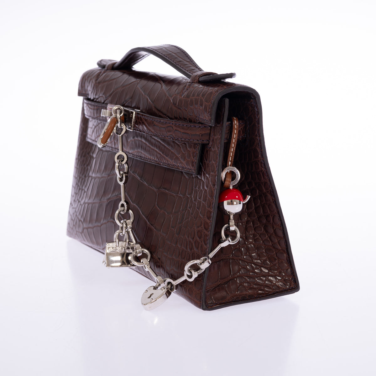 Hermès Kelly Pochette in Havane matte alligator, three-quarter view styled with charms sold separately.