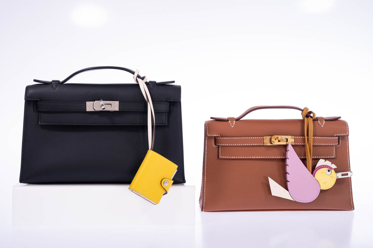 Hermès Kelly Pochette Noir Swift Palladium Hardware, beside a second Kelly Pochette with charms, all sold separately