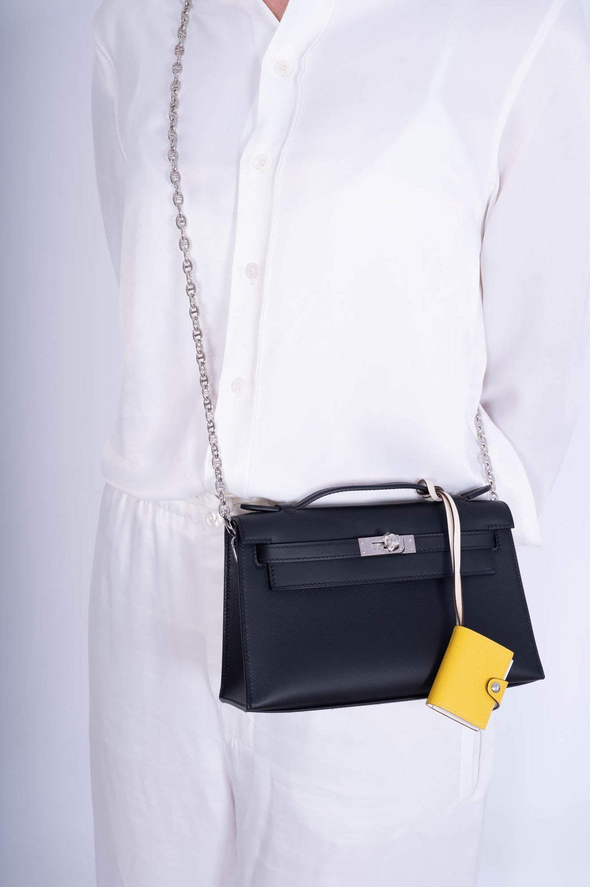 Hermès Kelly Pochette Noir Swift Palladium Hardware, worn crossbody on a chain by a model, chain and charm sold separately