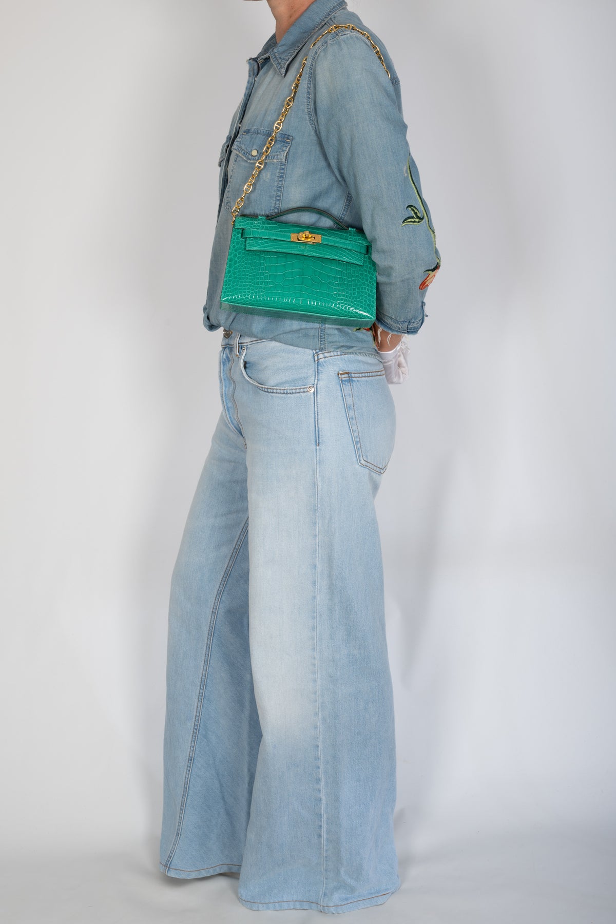 Hermès Kelly Pochette in Vert Jade shiny alligator with gold hardware, styled on a model with a gold-tone chain.