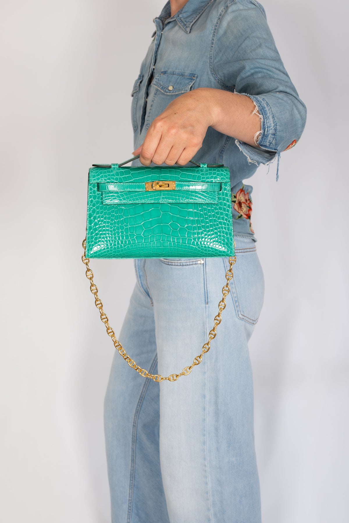 Hermès Kelly Pochette in Vert Jade shiny alligator with gold hardware, close hand-carried view with chain styling.