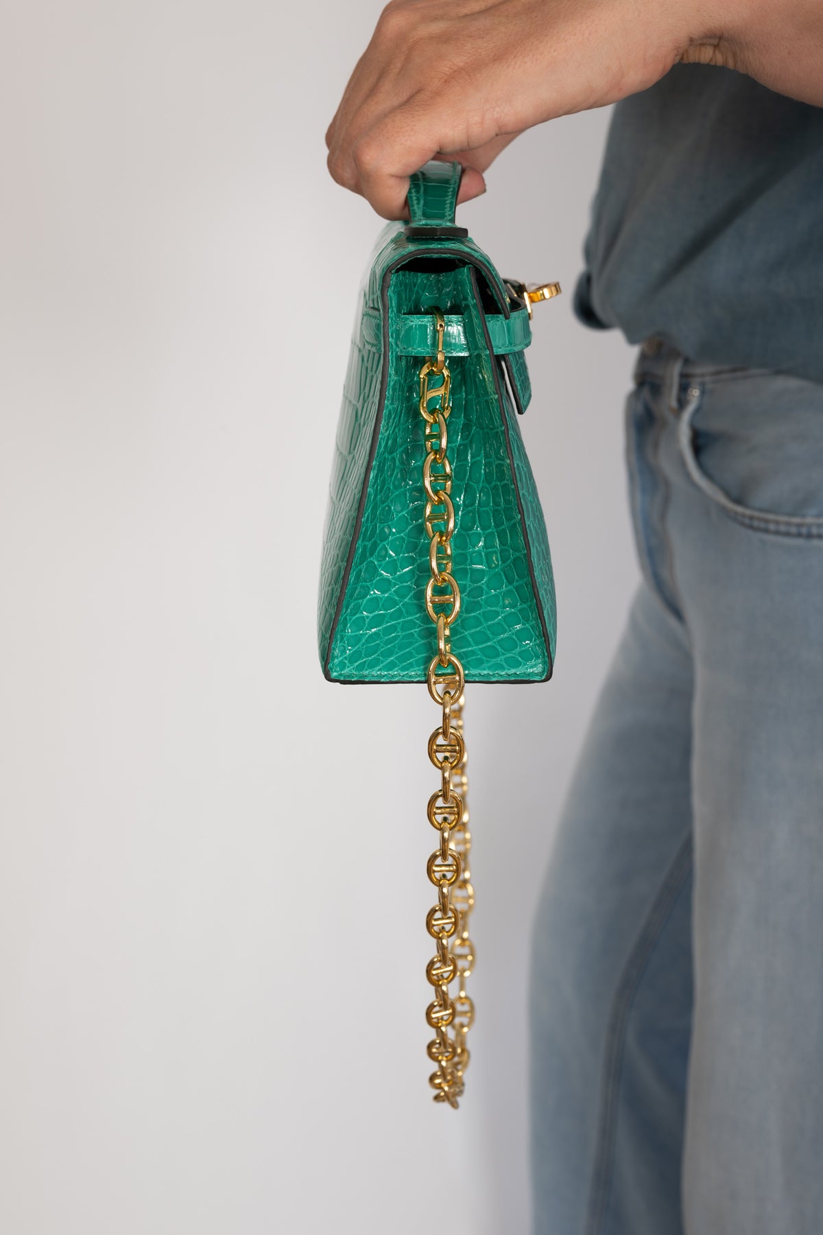 Hermès Kelly Pochette in Vert Jade shiny alligator with gold hardware, hand-carried side profile showing the gusset and chain.