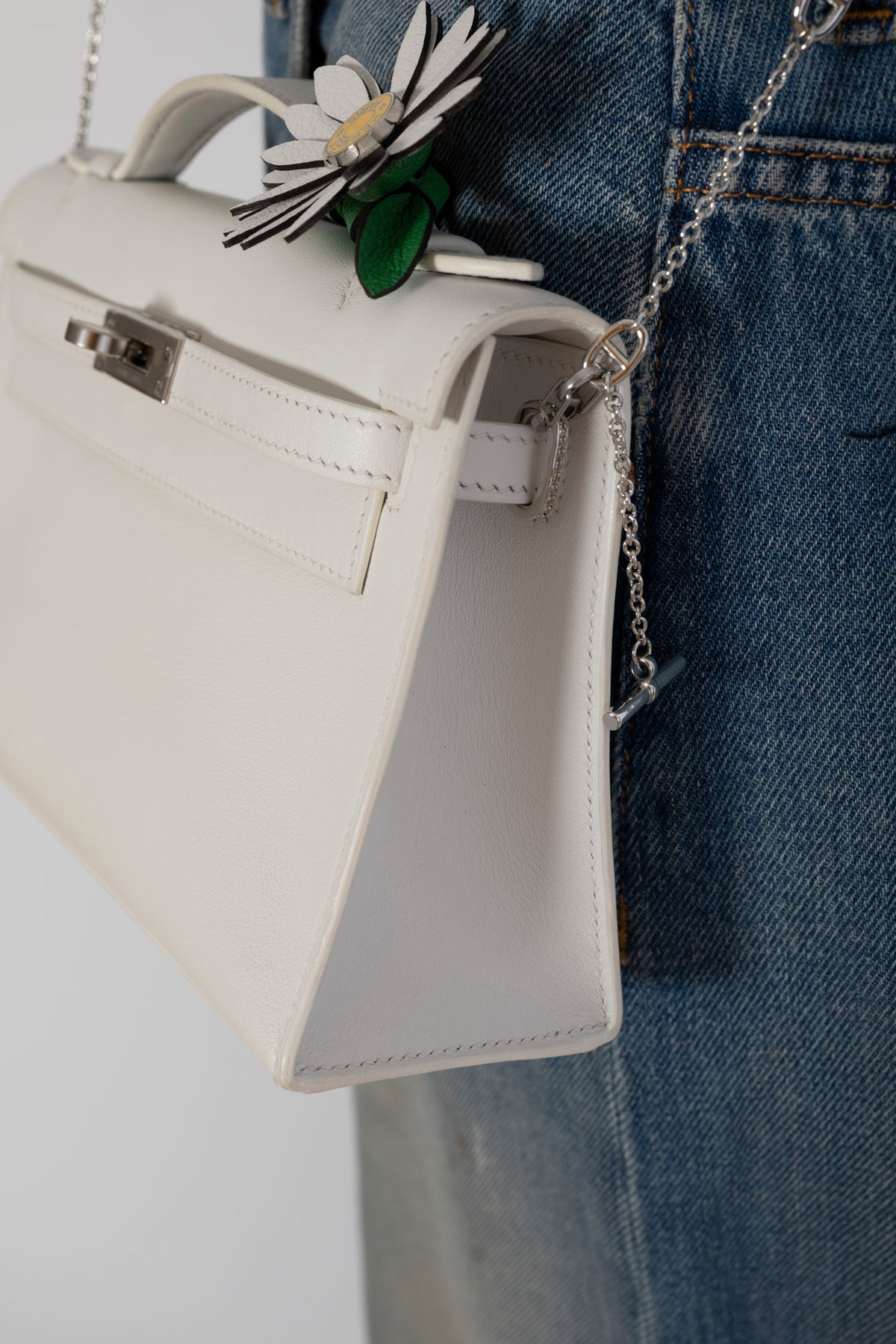 Hermès Kelly Pochette White Swift Palladium Hardware, worn on a chain by a model, close view, styled with a daisy charm, sold separately