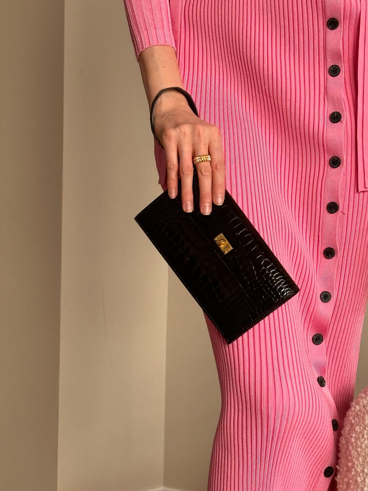 Hermès Kelly Pocket Long Wallet Black Alligator Gold Hardware, held by a model in a pink knit dress