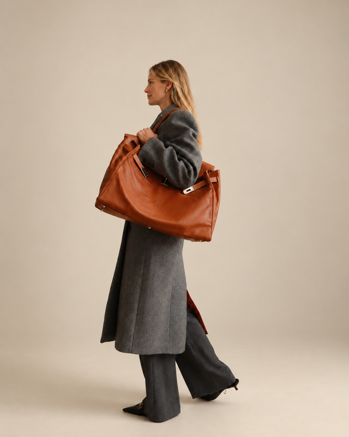 Hermès Kelly Relax 50 Fauve Swift Palladium Hardware, carried on the shoulder by a model in a gray coat, full-length view