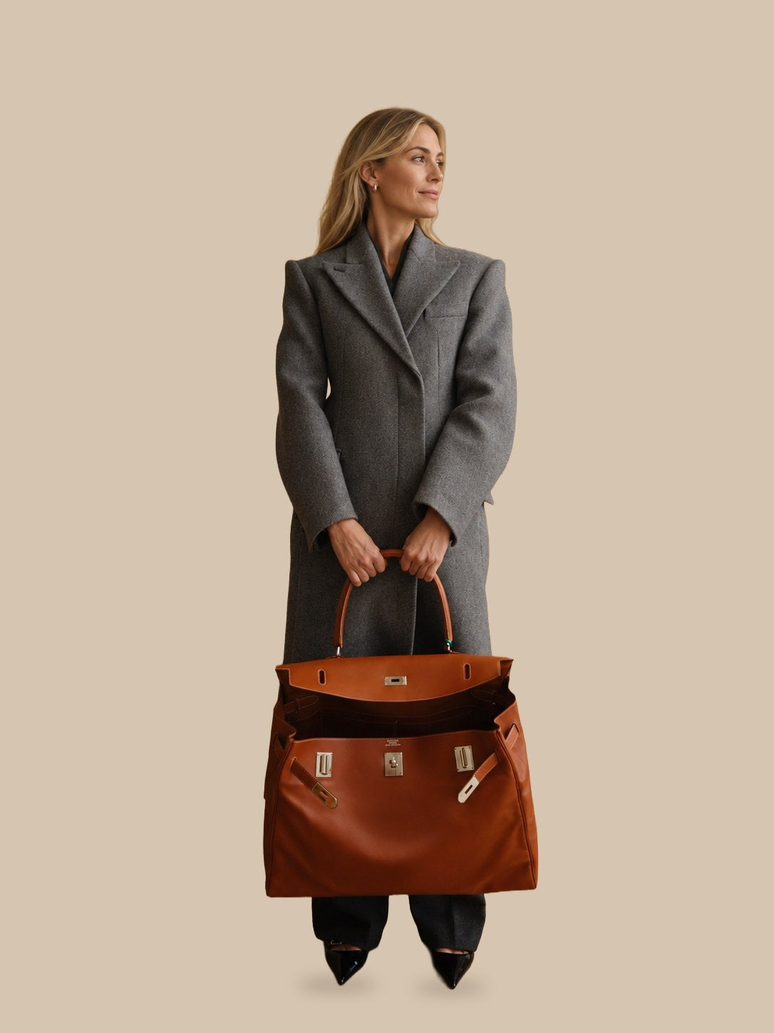 Hermès Kelly Relax 50 Fauve Swift Palladium Hardware, held in front with both hands by a model in a gray coat
