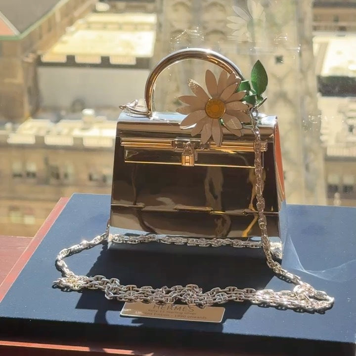 Hermès Marguerite Daisy Charm White Jaune de Naples Bambou, on the handle of a silver mini Kelly with a chain, bag and chain sold separately