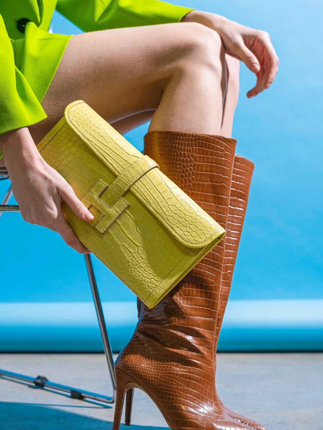 Hermès Verso Jige Élan Lime Matte Alligator and Caramel, held against the knee by a seated model in tall boots
