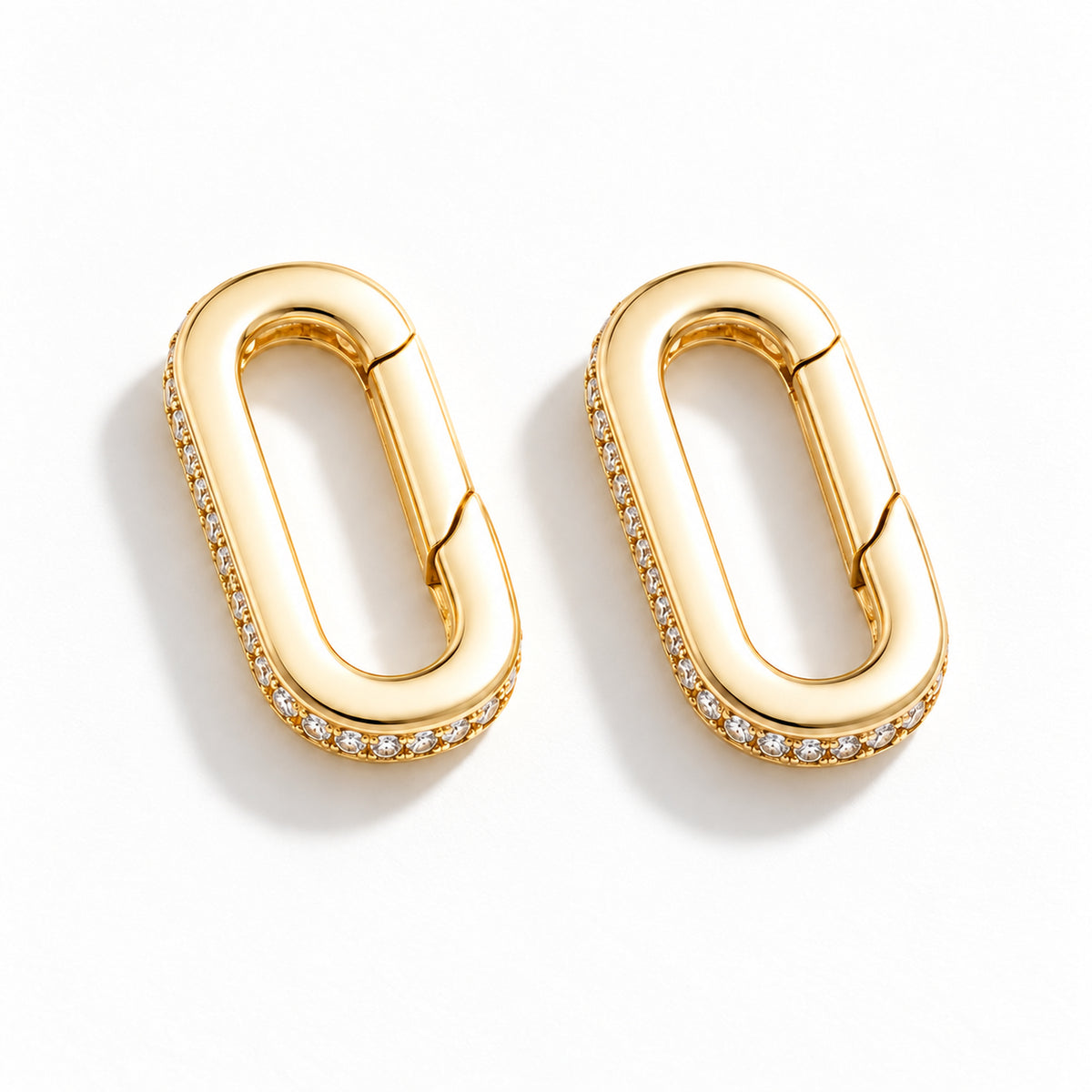 The Strap Converter, two gold-plated oval spring-gate converters with clear stone detailing, shown as a pair on white.