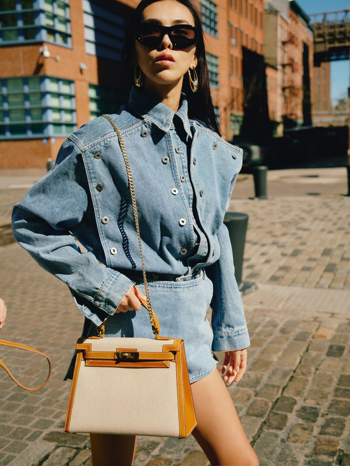 Vintage Hermès Kelly 28 Sellier Naturel and Écru Toile H and Peau Porc Gold Hardware, carried on a chain by a model on a cobblestone street
