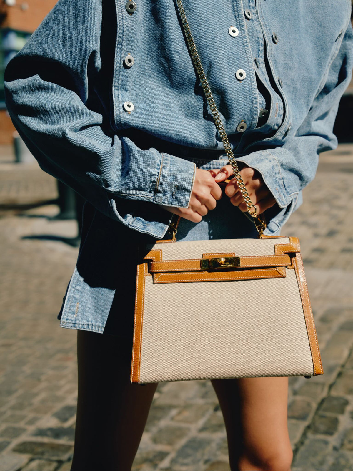 Vintage Hermès Kelly 28 Sellier Naturel and Écru Toile H and Peau Porc Gold Hardware, held on a chain by a model, close view