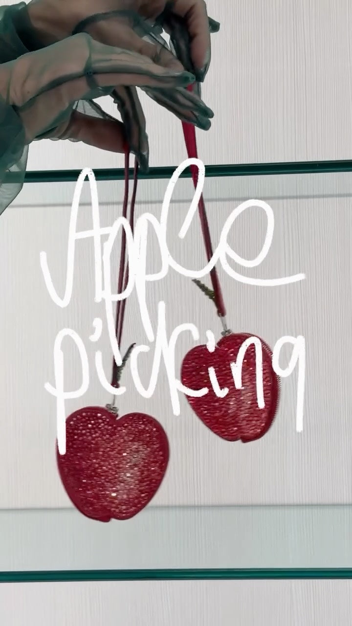 Two red apple bag charms against a glass shelf