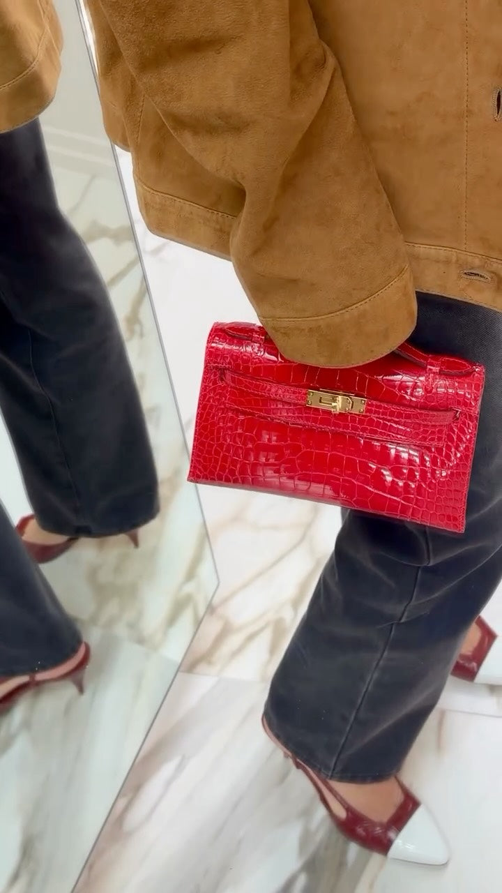 A red exotic Hermès Kelly Pochette carried in hand