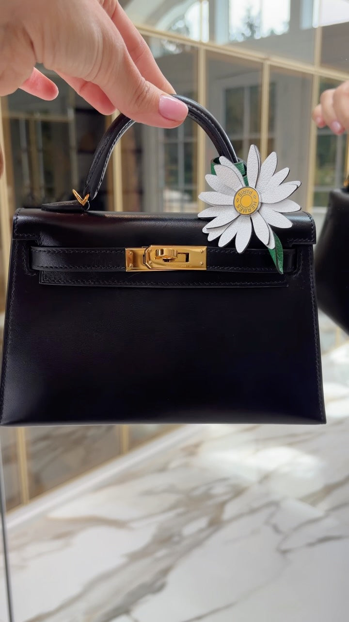JANEFINDS Instagram: Hand holding a small black top-handle bag with gold hardware and a white daisy charm