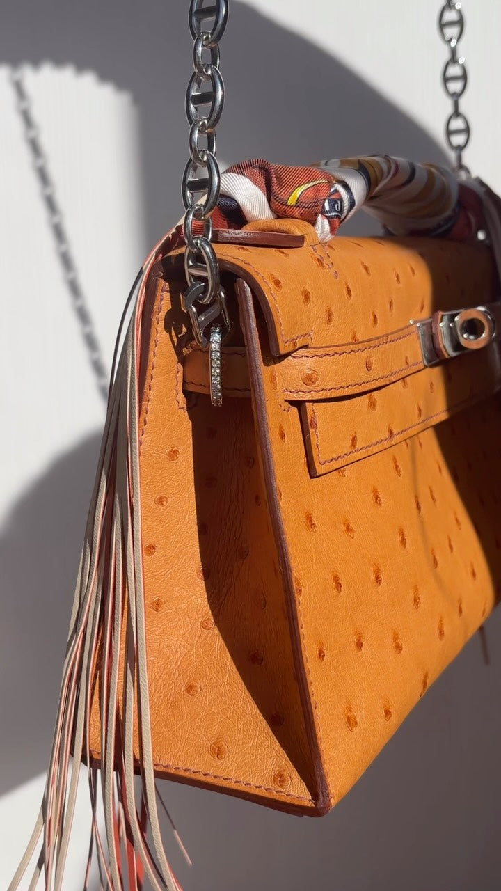 JANEFINDS Instagram: Orange top-handle bag hanging from a silver chain strap, with a printed scarf on the handle and a long fringe tassel