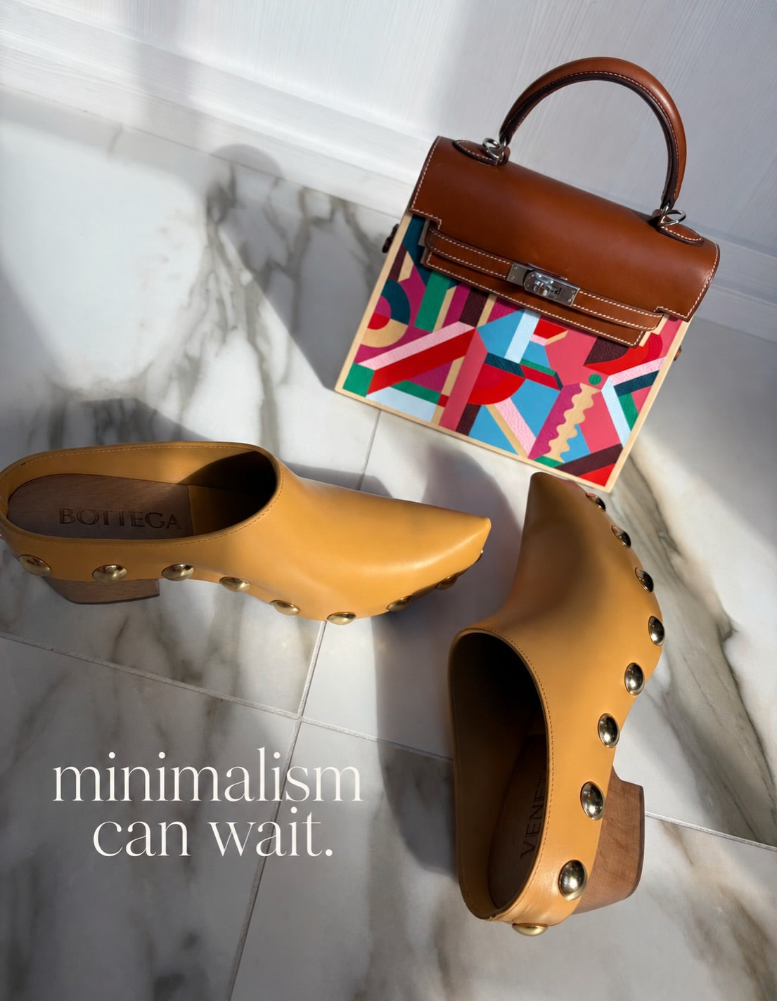 JANEFINDS Instagram: Hermès top-handle bag with a brown leather flap and colorful geometric panel beside studded tan clogs on a marble floor
