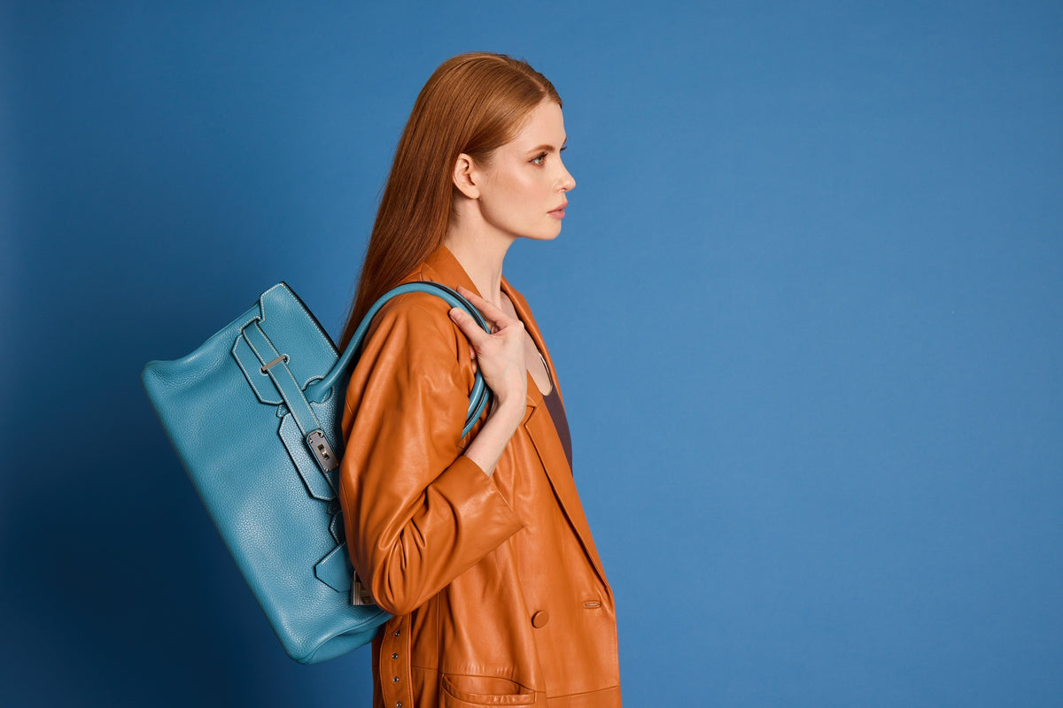 Hermès Shoulder Birkin 42 in Bleu Jean Togo with palladium hardware, carried on the shoulder by a model in a cognac leather coat